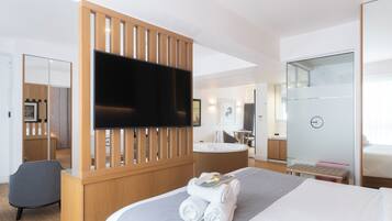 Una habitación de hotel moderna con una cama grande, un televisor de pantalla plana, un separador de madera, una zona de estar y un baño con puerta de vidrio.