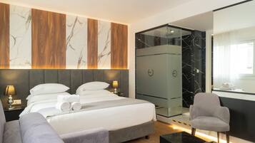 Quarto de hotel moderno com uma cama grande, um sofá, um closet envidraçado e um banheiro com um espelho amplo.