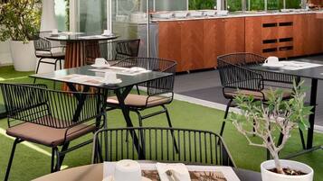 An outdoor dining area with tables and chairs, a buffet counter, and a potted plant.