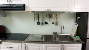 Een keuken met witte kastjes, een RVS spoelbak en verschillende keukengerei dat aan de muur hangt.