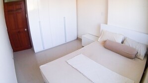 Een slaapkamer met een bed, een kledingkast, een nachtkastje en een klok aan de muur.