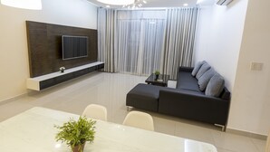 A modern living room with a flat-screen TV, a black sofa, a dining table with chairs, and a potted plant. - Cozzy and Beauty Apartment (Ho Chi Minh City)