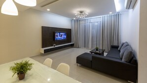 A modern living room with a flat-screen TV, a sofa, a dining table with chairs, and a potted plant. - Cozzy and Beauty Apartment (Ho Chi Minh City)