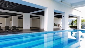 A swimming pool with clear blue water, surrounded by white pillars and a covered area with lounge chairs.