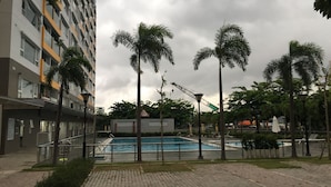 En boligbygning med swimmingpool omgivet af palmer og en byggekran i baggrunden.
