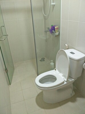 A bathroom with a glass-enclosed shower, a white toilet, and a small shelf with toiletries. - Bridge View Apartment (Ho Chi Minh City)