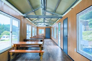 A long corridor with wooden benches, large windows, and a metal roof structure.