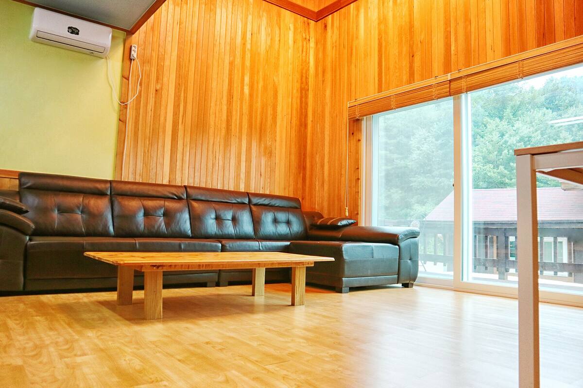 A living room with a brown leather sofa, a wooden coffee table, and a large sliding glass door leading to an outdoor area.