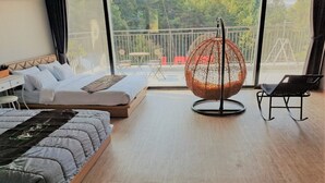 Un dormitorio moderno con cama, sillón colgante y balcón con vistas a árboles.