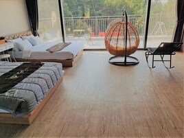 A modern bedroom with a bed, a hanging chair, and a balcony with a view of trees.