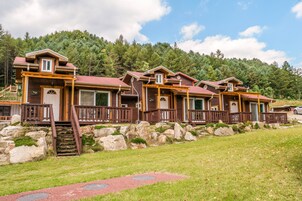 A row of cabins with wooden exteriors, stone foundations, and a grassy lawn.