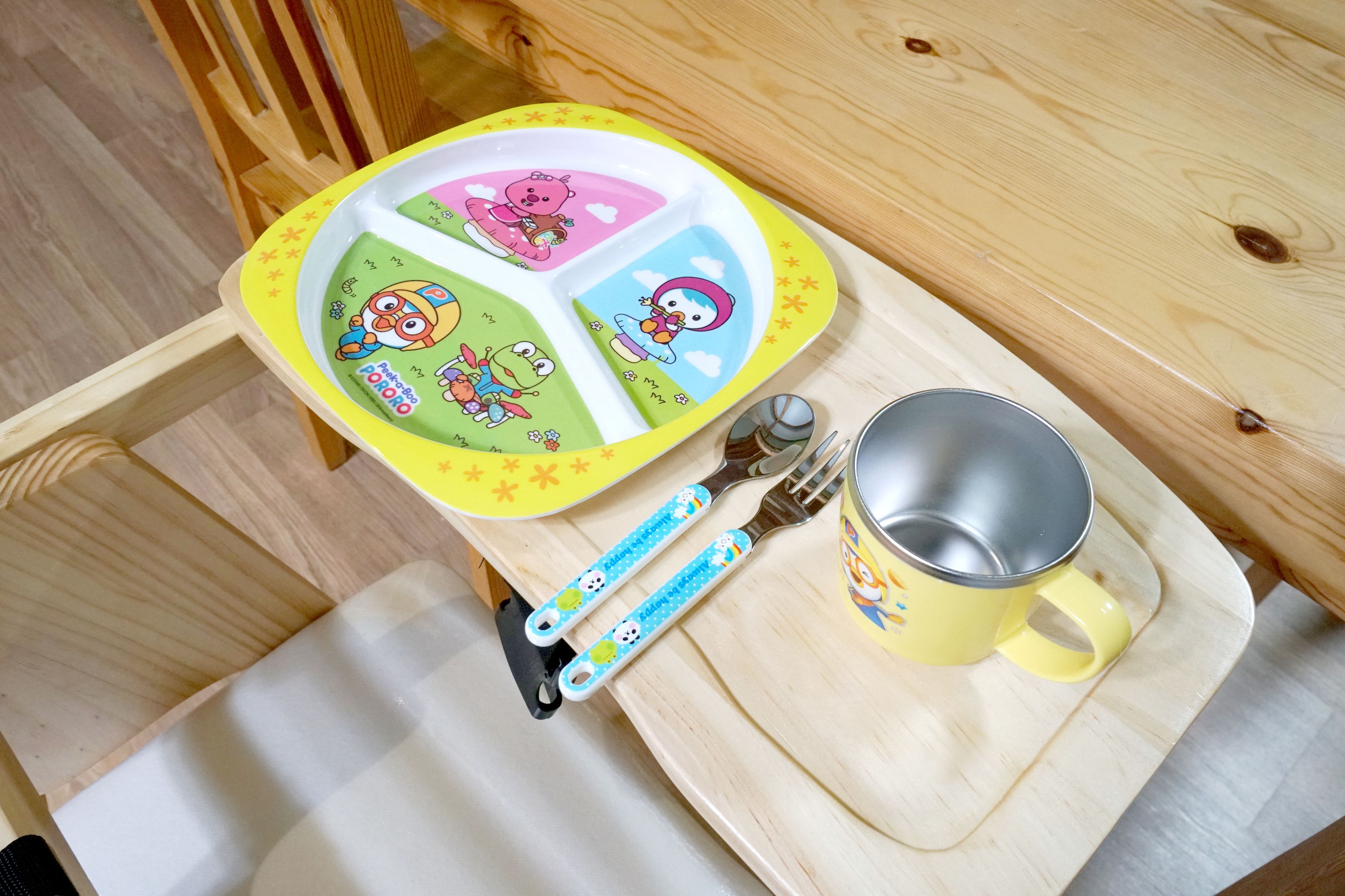 A wooden table with a yellow tray, a mug, and a fork with a cartoon design.