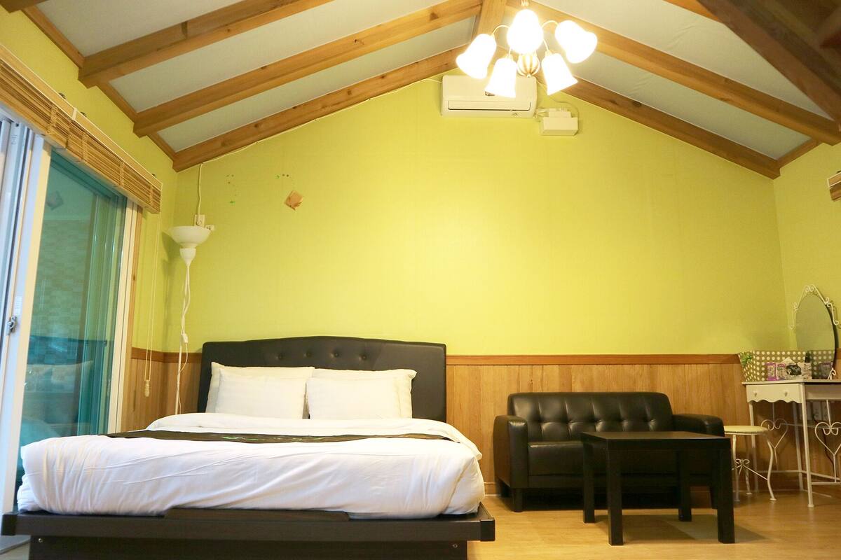 A bedroom with a bed, a chair, a desk, and a mirror.
