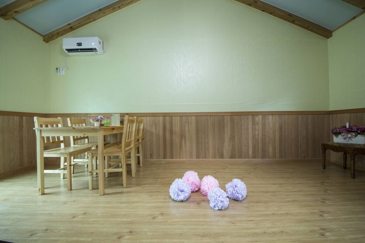A room with a wooden floor, a dining table with chairs, and a small table with flowers.