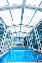 A glass-enclosed swimming pool with clear blue water, surrounded by a white and blue frame structure.