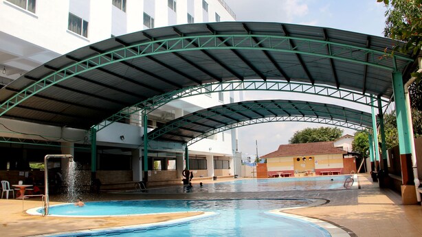 A swimming pool with a covered area and a building in the background.