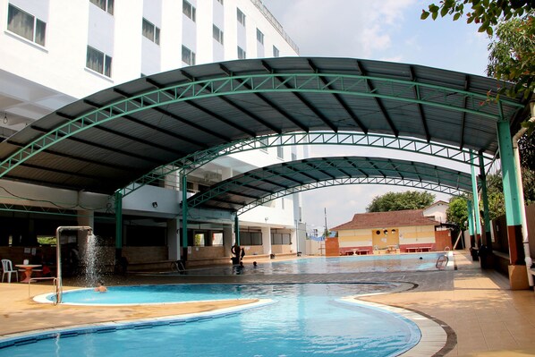 A swimming pool with a covered area and a building in the background.