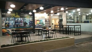 An indoor seating area with tables and chairs, a counter with a menu, and a wall with posters. - Hotel ASRC (Alor Setar)