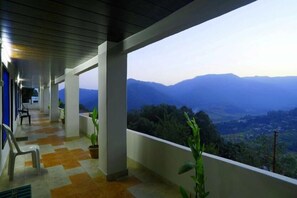 A covered balcony with a view of a valley and mountains. - Hotel Kausani Retreat (Somashwar)
