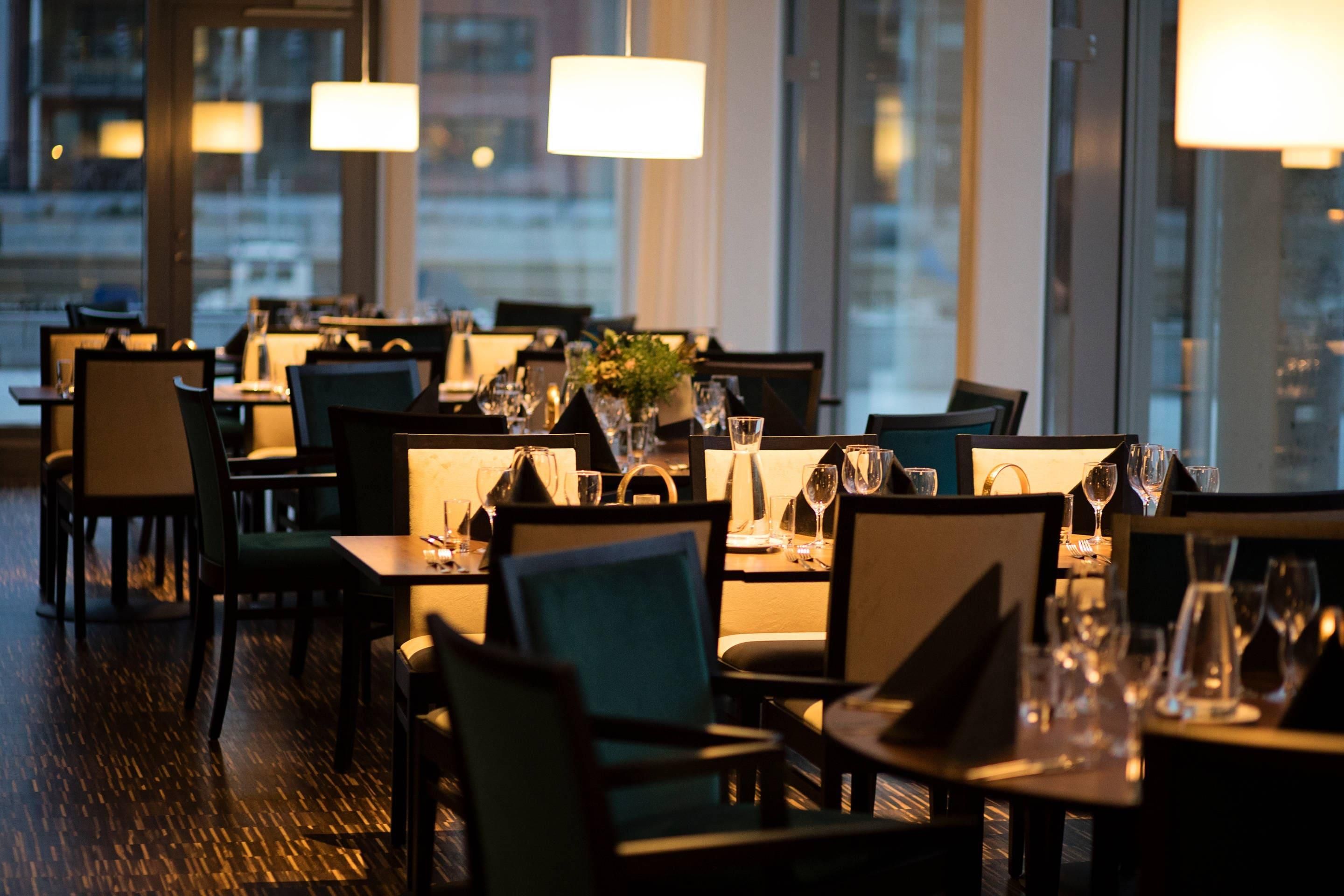 A restaurant with tables set for dining, chairs, and a view of the cityscape through large windows.