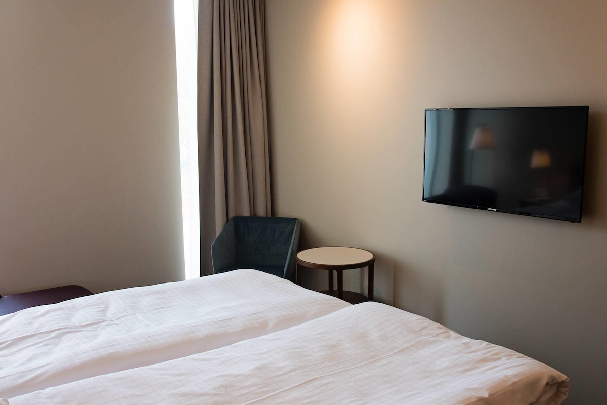 A hotel room with a bed, a chair, a small round table, and a wall-mounted television.