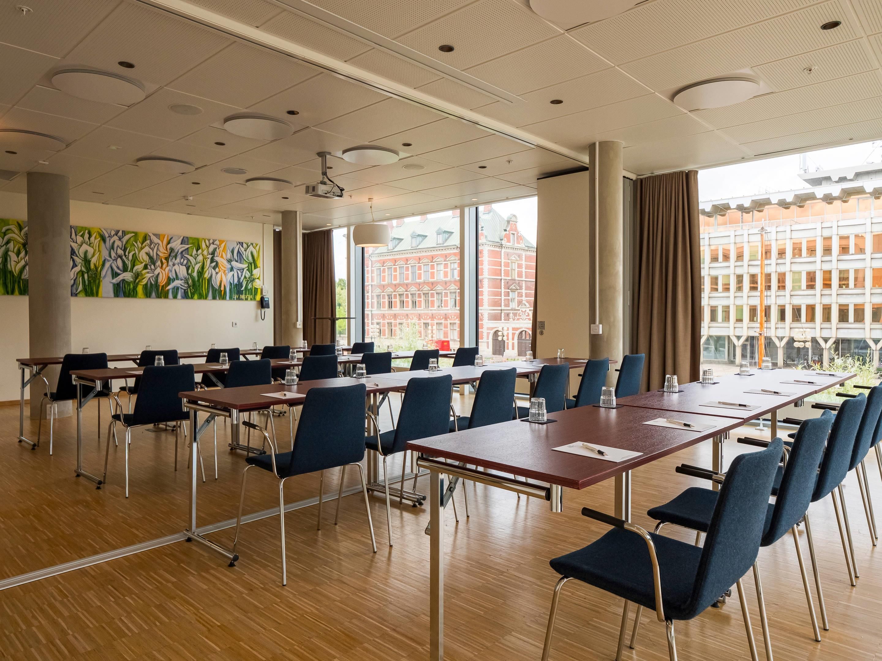 A conference room with tables and chairs, large windows, and a view of buildings.