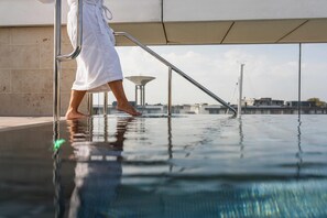 A person in a white bathrobe stepping into a pool with a metal railing and a clear view of the sky and buildings in the background. - Quality Hotel Öresund (Landskrona)