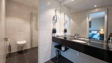 A modern bathroom with a large mirror, two sinks, a toilet, and a shower.