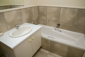 A bathroom with a sink and bathtub, beige tiles, and a mirror above the sink. - Villa 5 (Knysna)