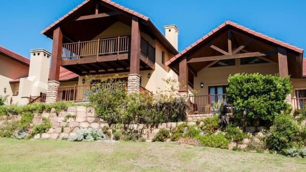 A two-story house with a balcony on the upper floor, stone foundation, and a well-maintained garden. - Villa 5 (Knysna)