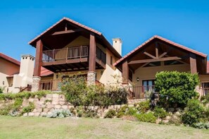 A two-story house with a balcony on the upper floor, stone foundation, and a well-maintained garden. - Villa 5 (Knysna)