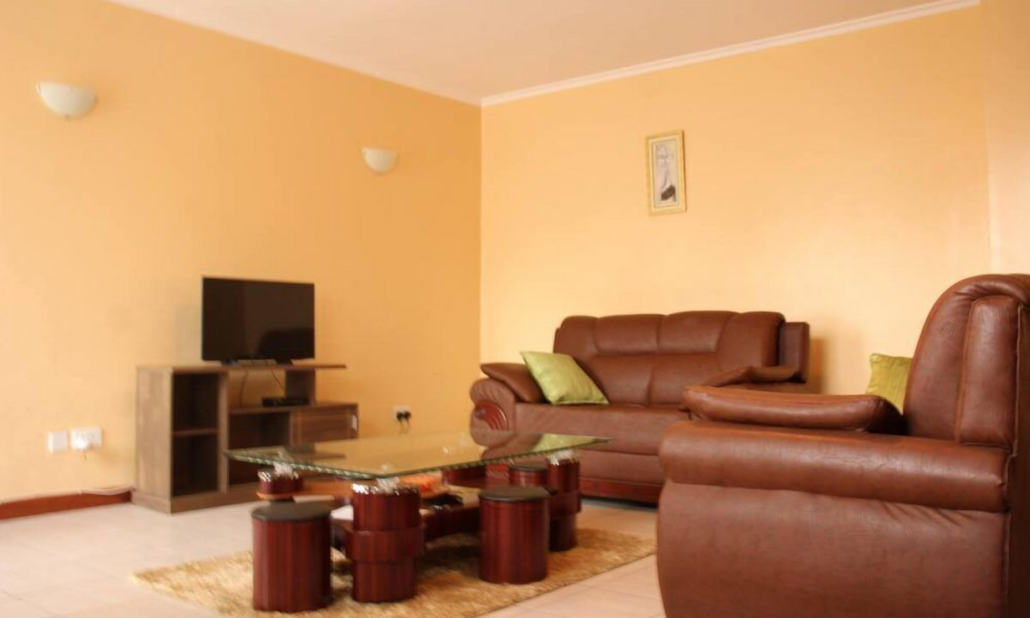 Una sala de estar con un sofá de cuero marrón, una mesa de centro de vidrio y un televisor sobre un soporte de madera.
