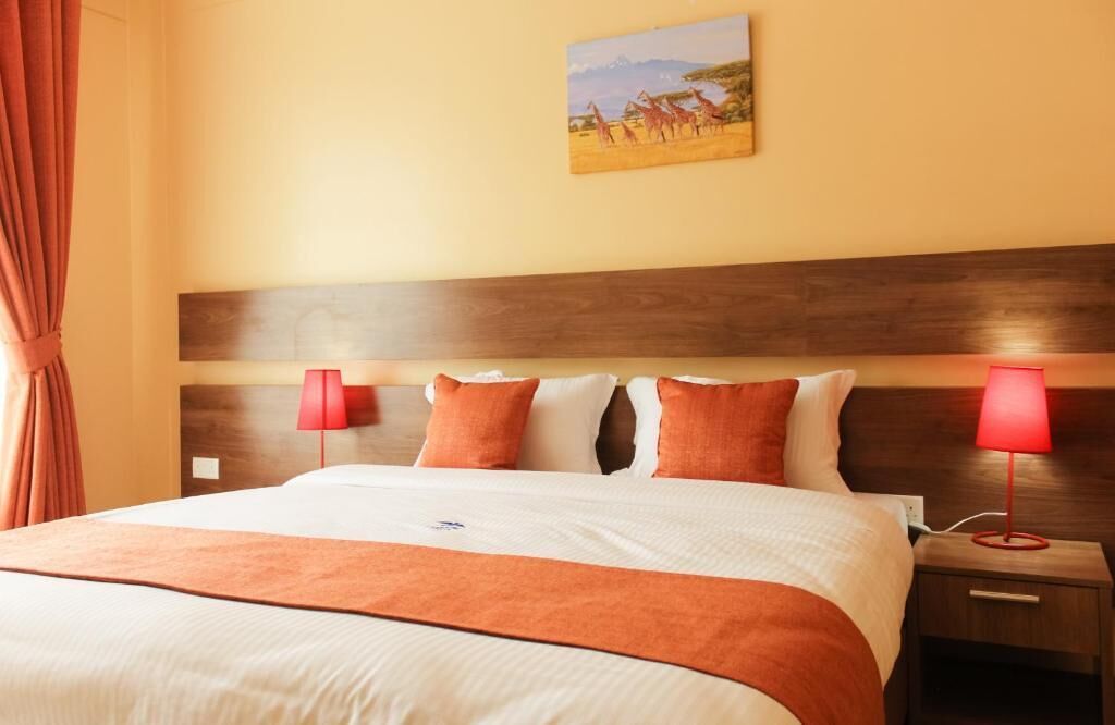 Habitación de hotel con una cama grande, dos mesitas de noche con lámparas, un cuadro en la pared y una ventana con cortinas.