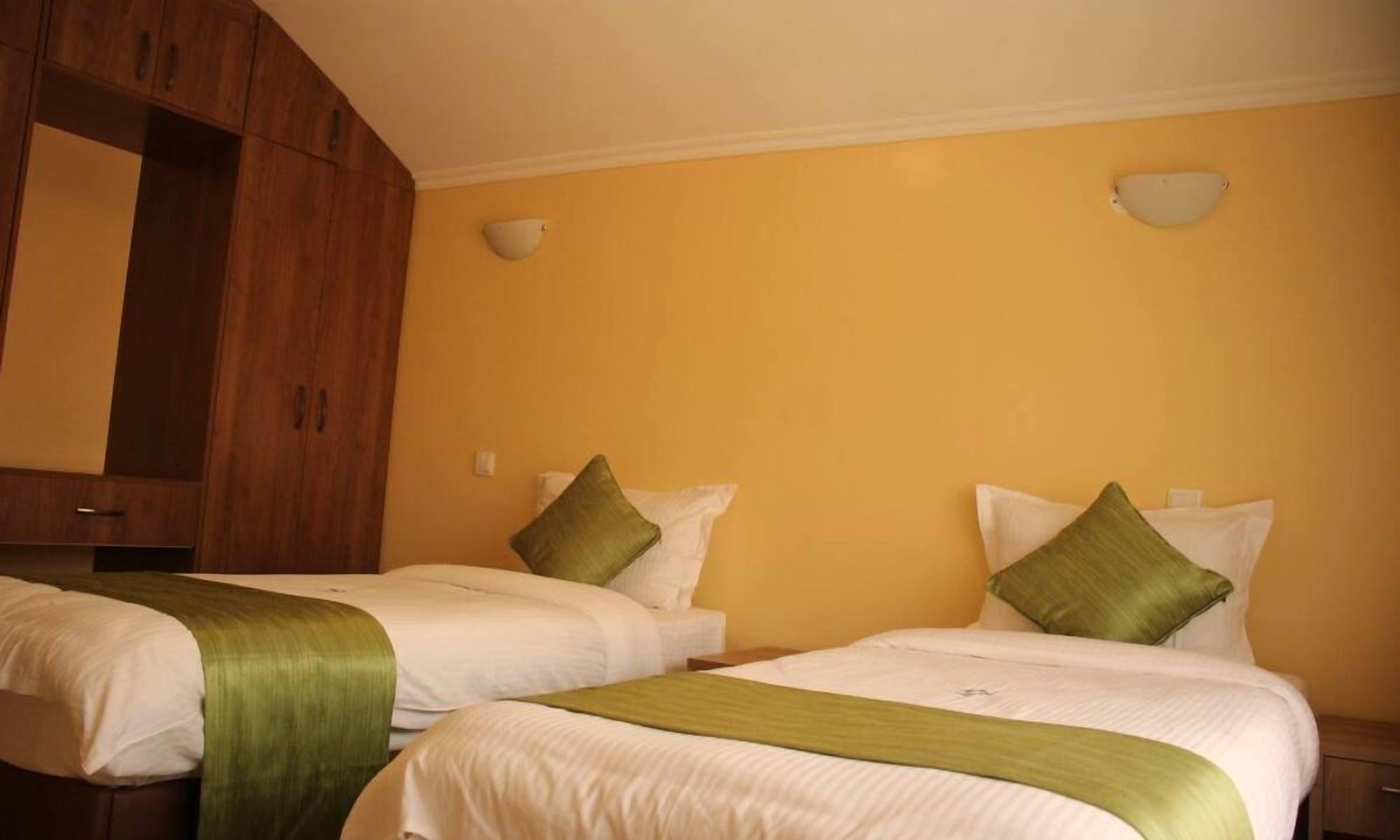 A hotel room with two beds, each with white bedding and green sashes, and wooden furniture.