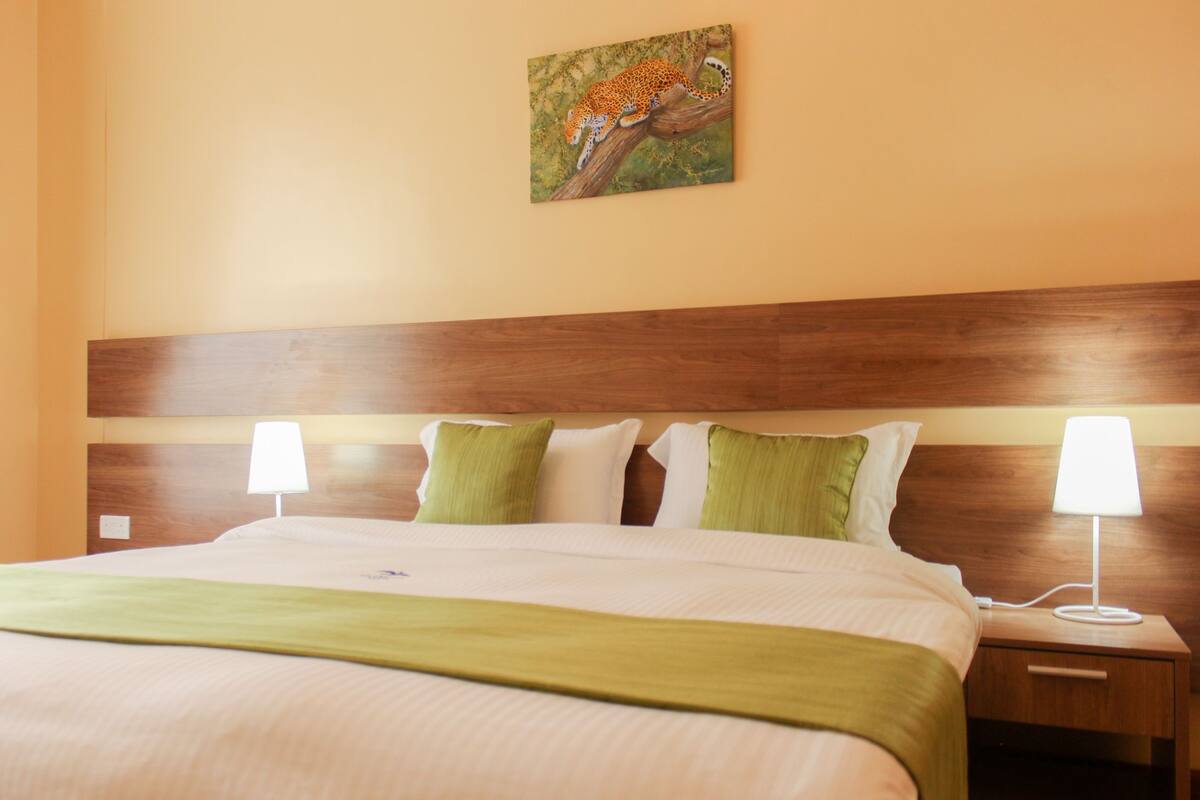 Ein Hotelzimmer mit einem großen Bett, zwei Nachttischlampen und einem Leopardenbild an der Wand.