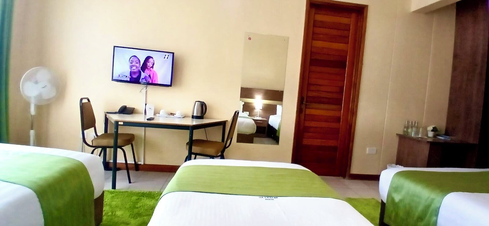 Ein Hotelzimmer mit zwei Betten, einem Schreibtisch, einem Stuhl, einem Fernseher und einem Spiegel.