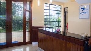 A reception area with a wooden reception desk, a large window with a view of greenery, and a sign indicating the location as a Lia Center in Kenya. - LIA Hotel & Training Centre (Nairobi)