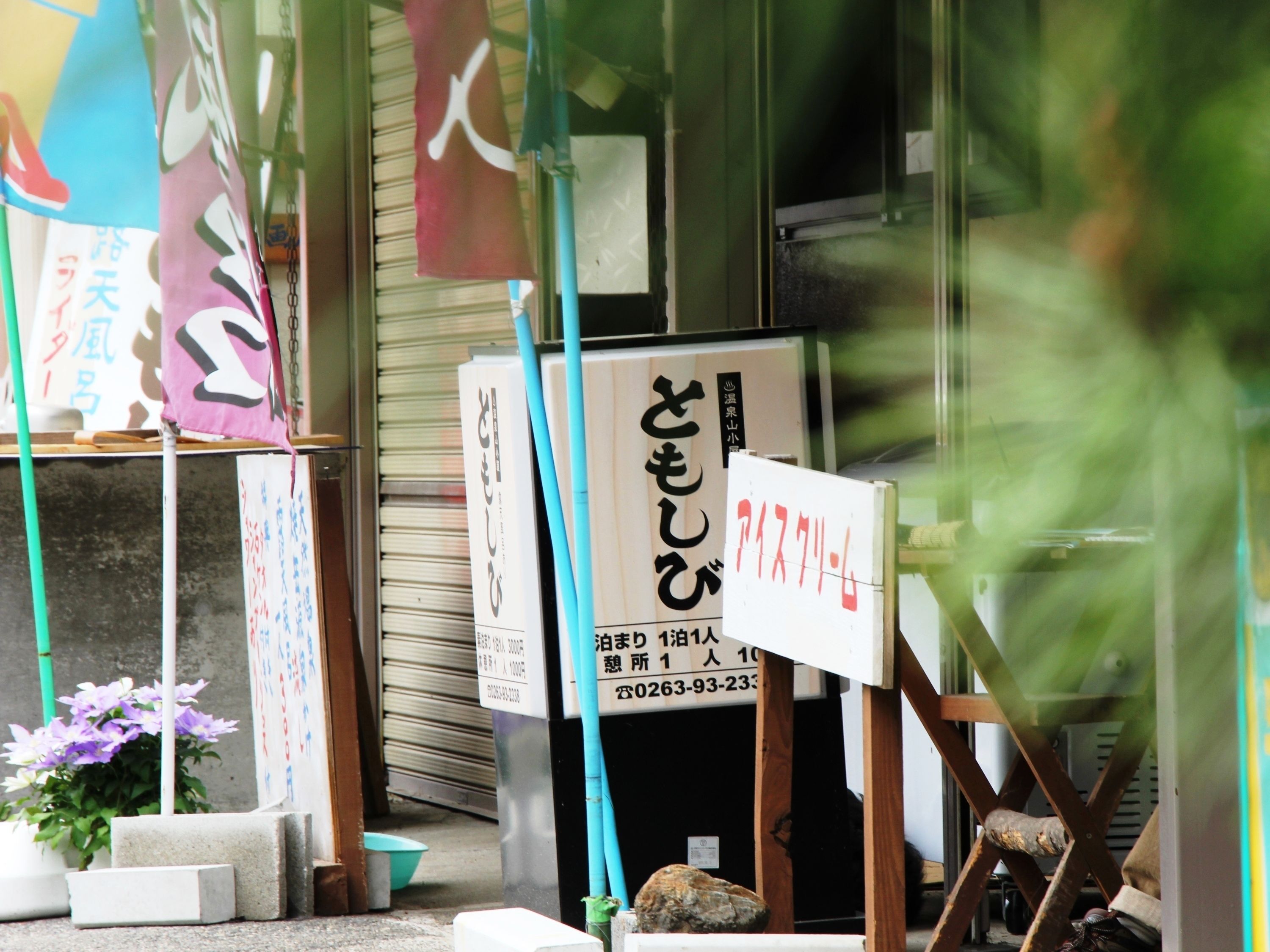 Une devanture de magasin ornée d’une enseigne japonaise, une porte à volets fermée et un pot de fleurs.