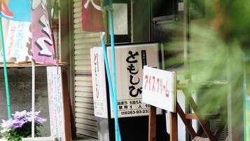 Une devanture de magasin ornée d’une enseigne japonaise, une porte à volets fermée et un pot de fleurs.