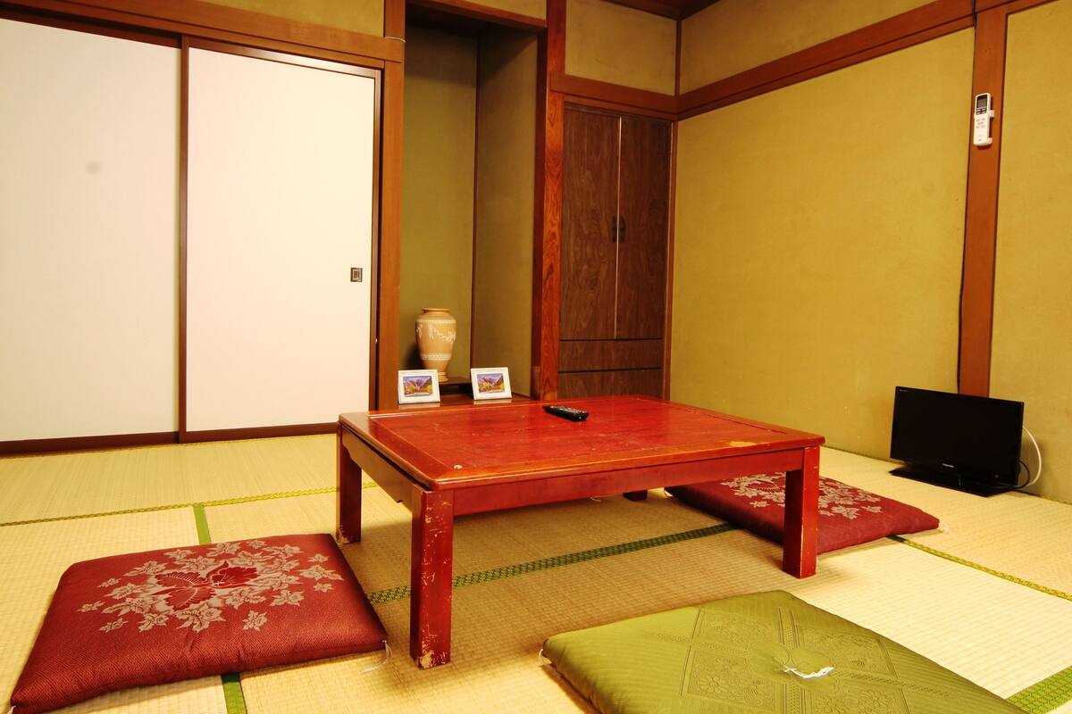 A traditional Japanese room with tatami flooring, a wooden table, and a red cushion.