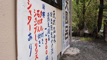 A sign with Japanese text on a building wall, surrounded by trees and gravel.