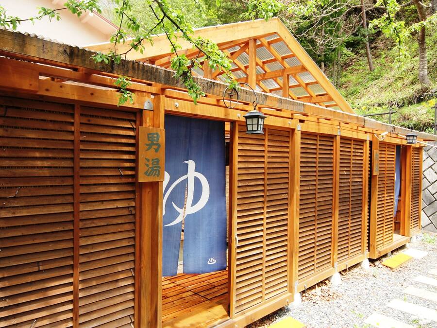 Une structure traditionnelle en bois, dotée d’un paravent de type shoji et d’une enseigne indiquant les toilettes pour hommes.