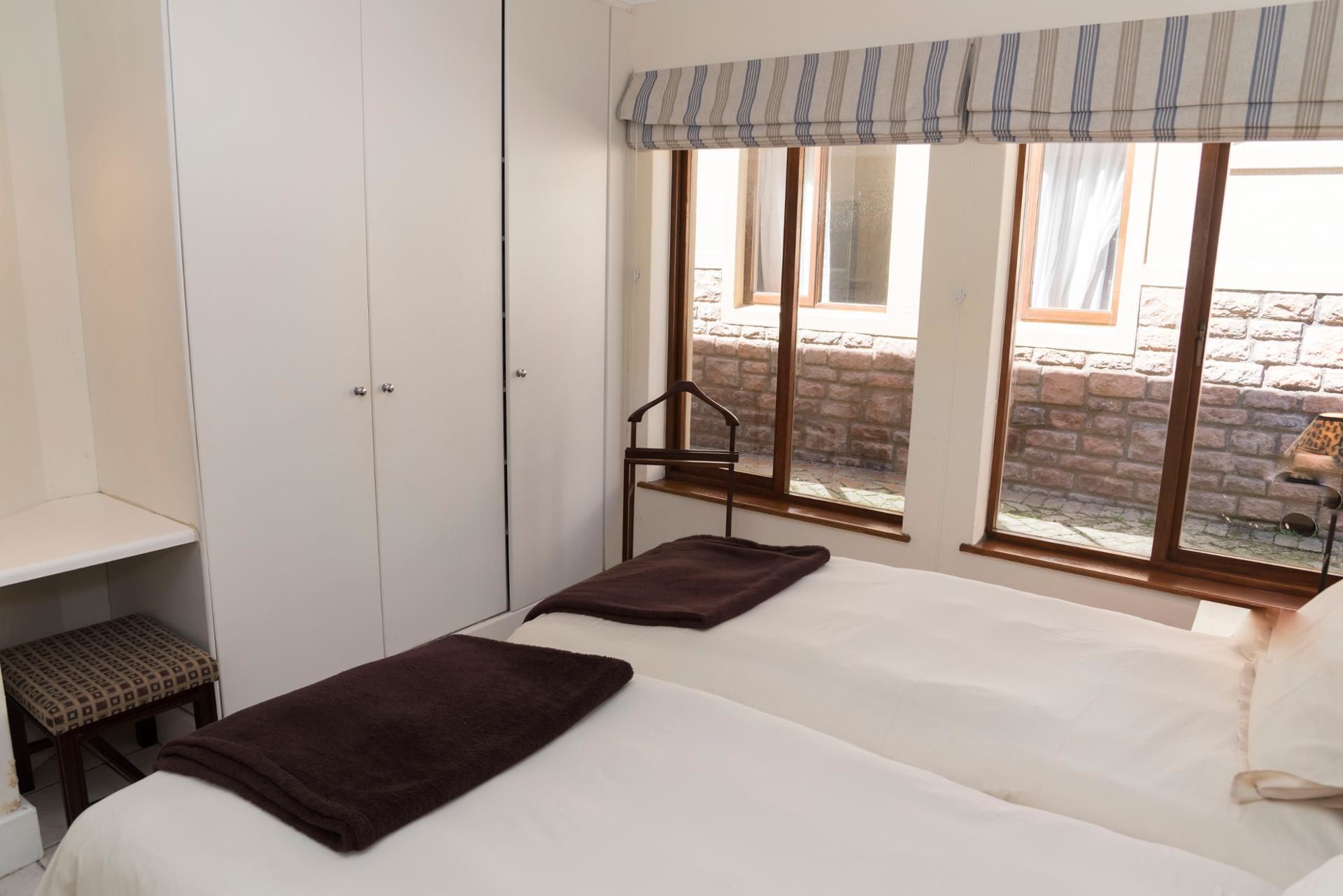 Un dormitorio con cama, armario, banco y ventana con vista a un muro de ladrillo y un edificio.
