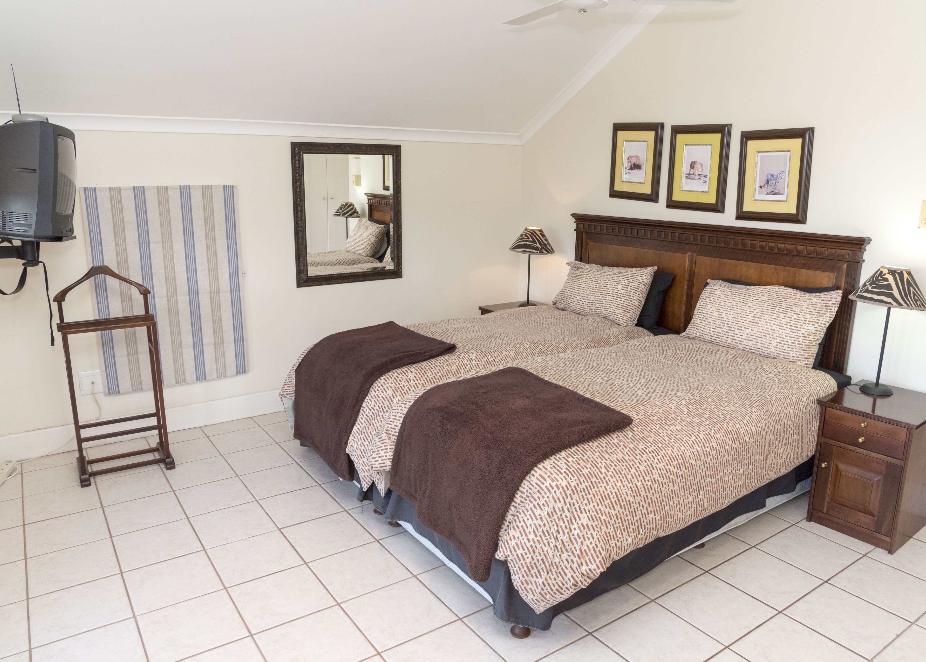 Quarto com uma cama grande, uma mesa de cabeceira de madeira, um criado-mudo, um espelho e um ventilador de teto.