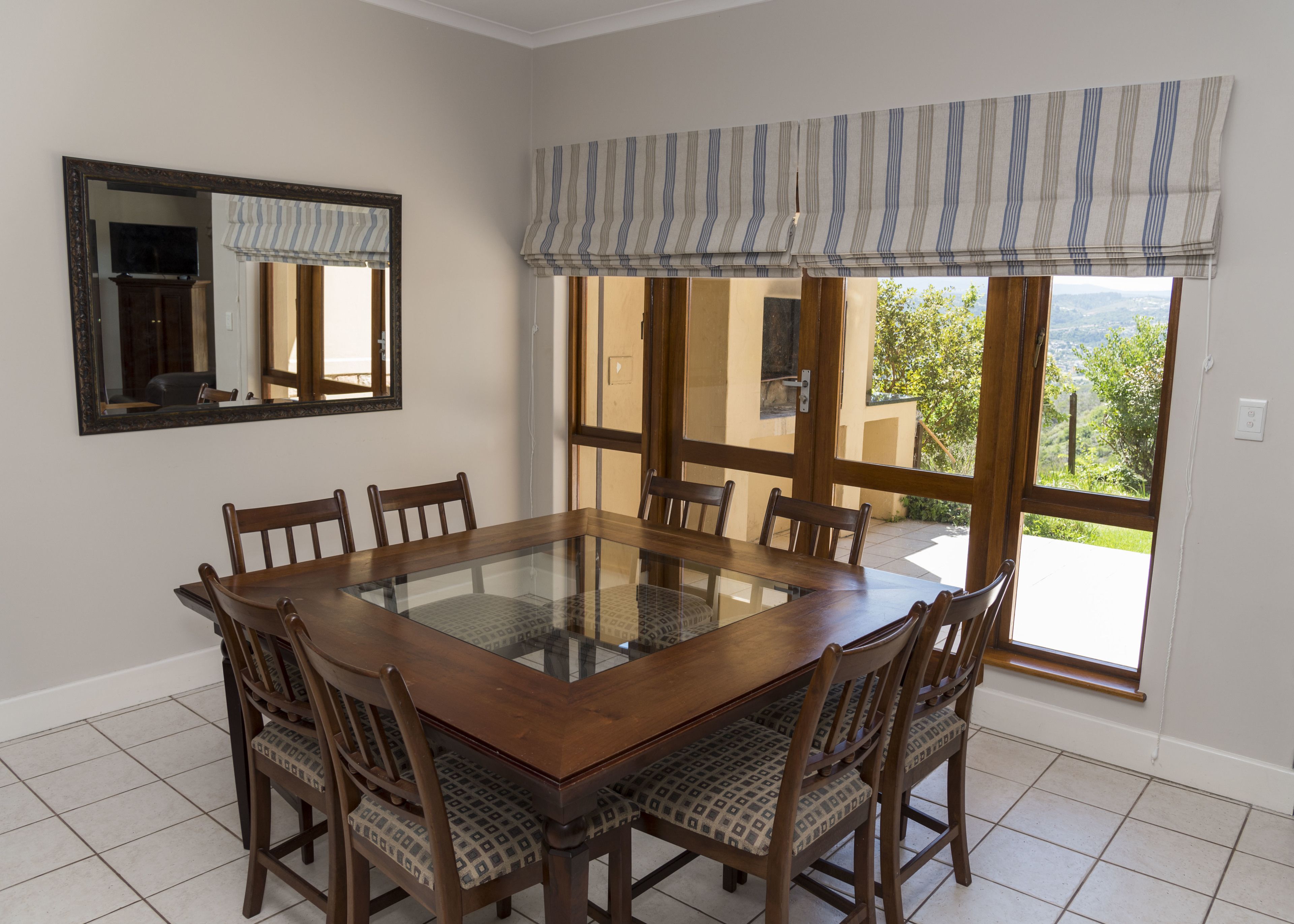 A dining area with a glass-top table surrounded by wooden chairs with patterned cushions.