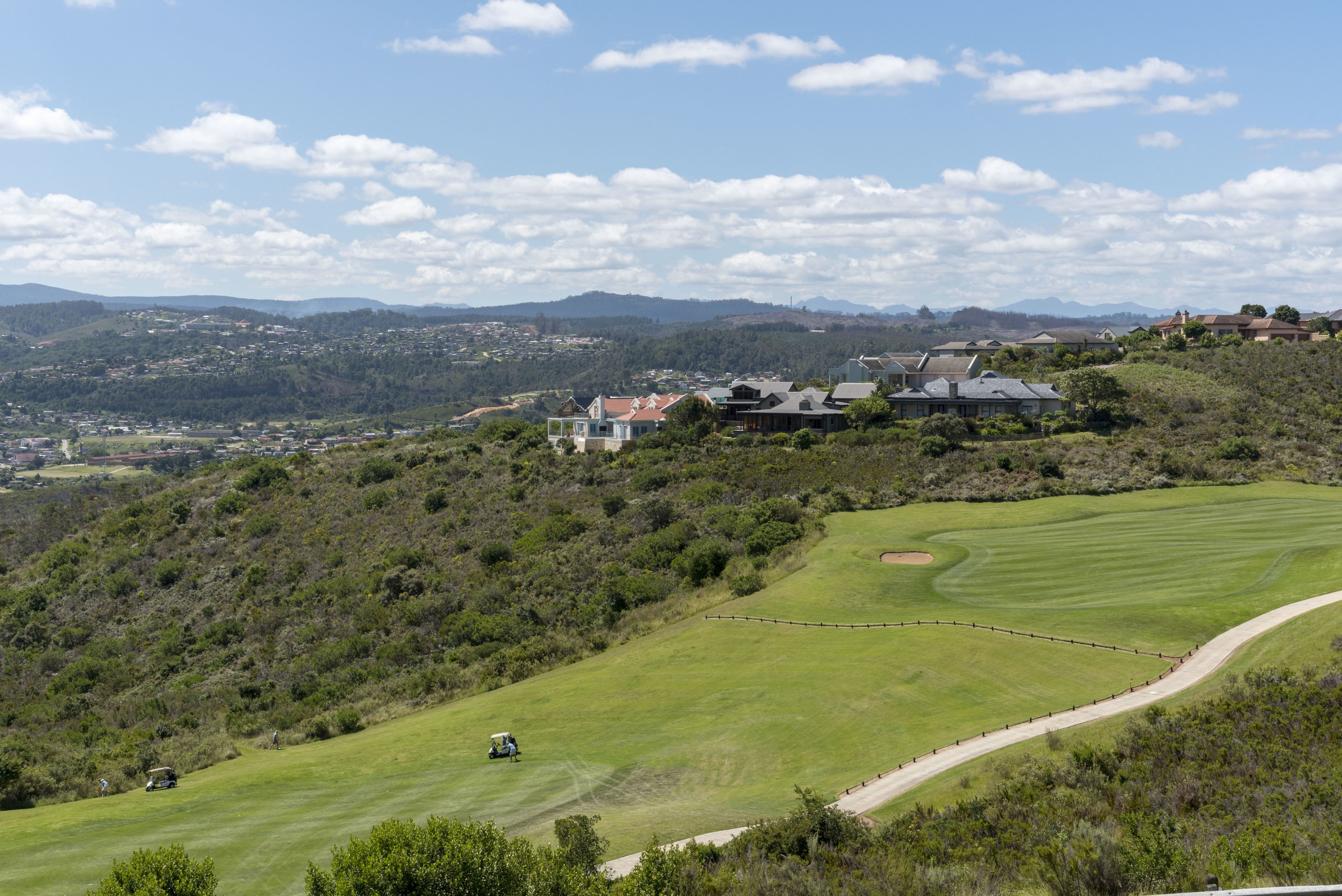 A golf course with a clubhouse, rolling hills, and distant mountains.