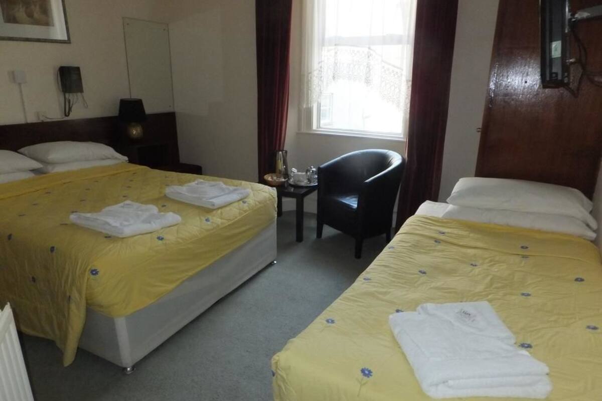 A hotel room with two beds, each with a yellow floral bedspread and white pillows. There is a small table with a lamp and a chair.