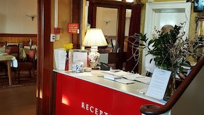 A reception area with a chandelier, a red sign reading "The Seaward Hotel Hotel - Bar - Restaurant", and a reception desk with a lamp and a vase of flowers.