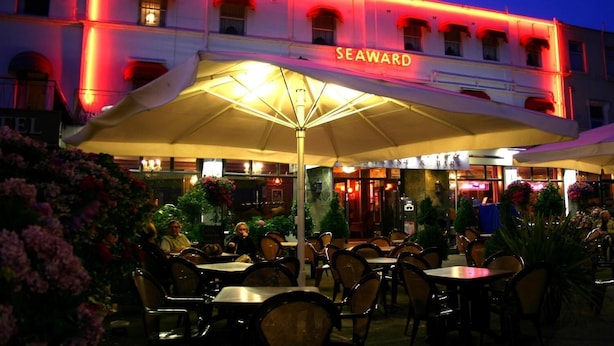 A building with the sign "SEAWARD" at the entrance, outdoor seating with umbrellas, and a well-lit facade.
