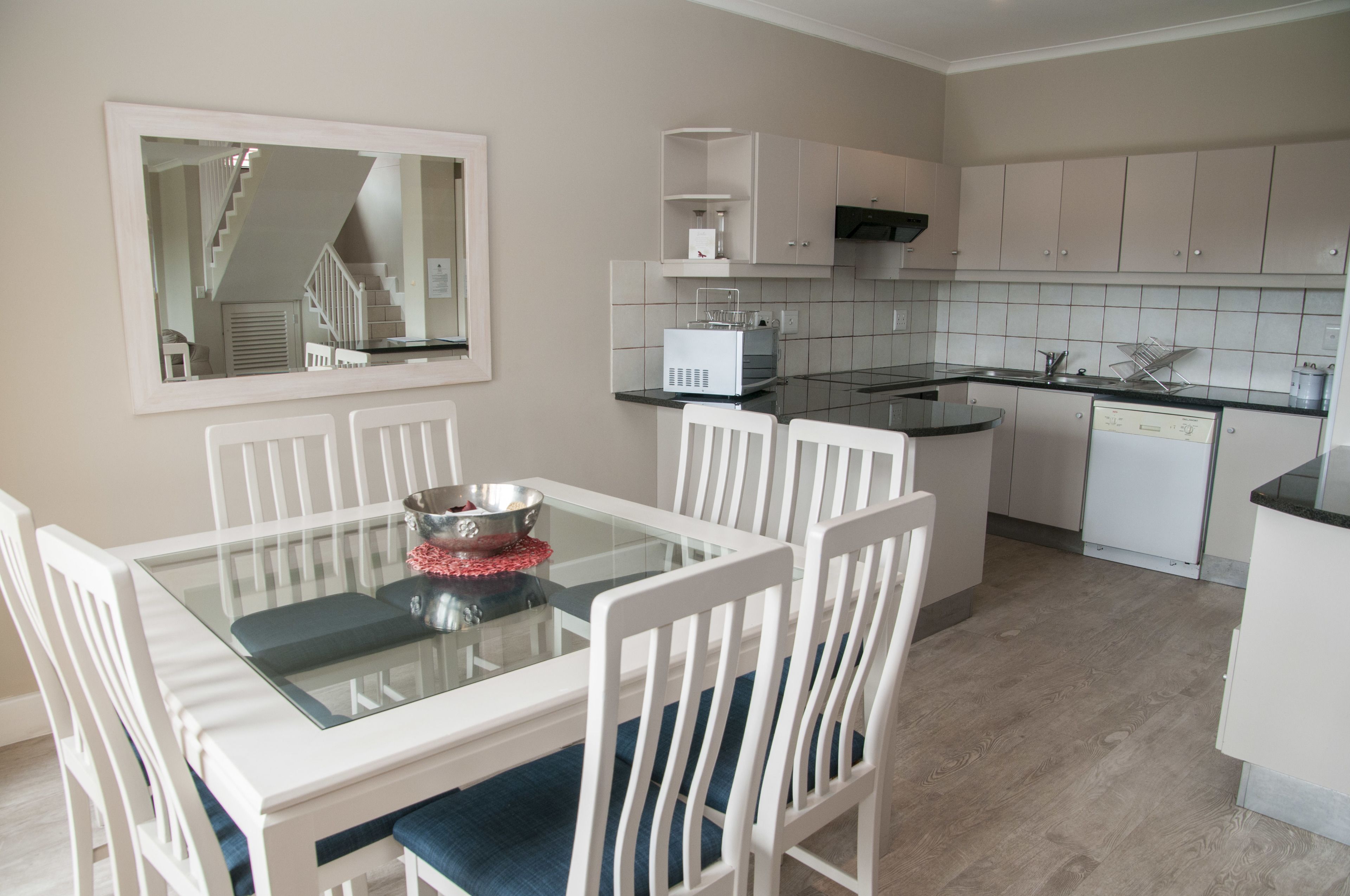 A modern kitchen with white cabinets, a glass dining table, and a built-in microwave.
